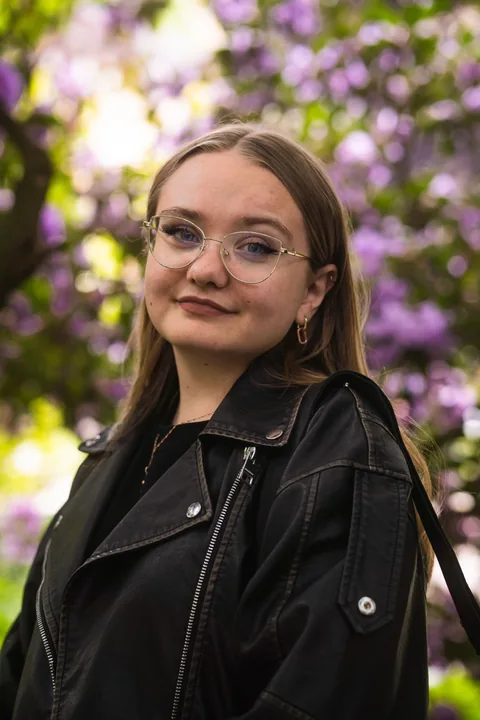 Portrait einer Frau mit Brille und Lederjacke vor violetten Blüten